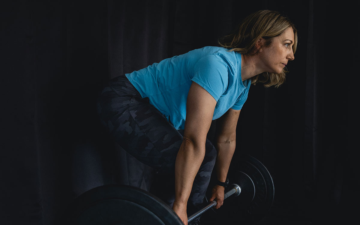 Woman in blue shirt lifting heavy weights on a barbell